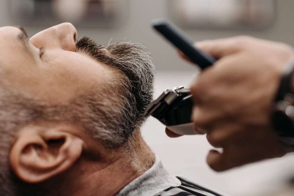 a-barber-cutting-a-client-s-beard-7518723 Close-up of a barber using clippers to groom a clients beard in a barbershop.