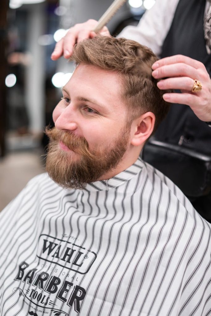 A stylish bearded man getting a haircut in a modern barbershop.
